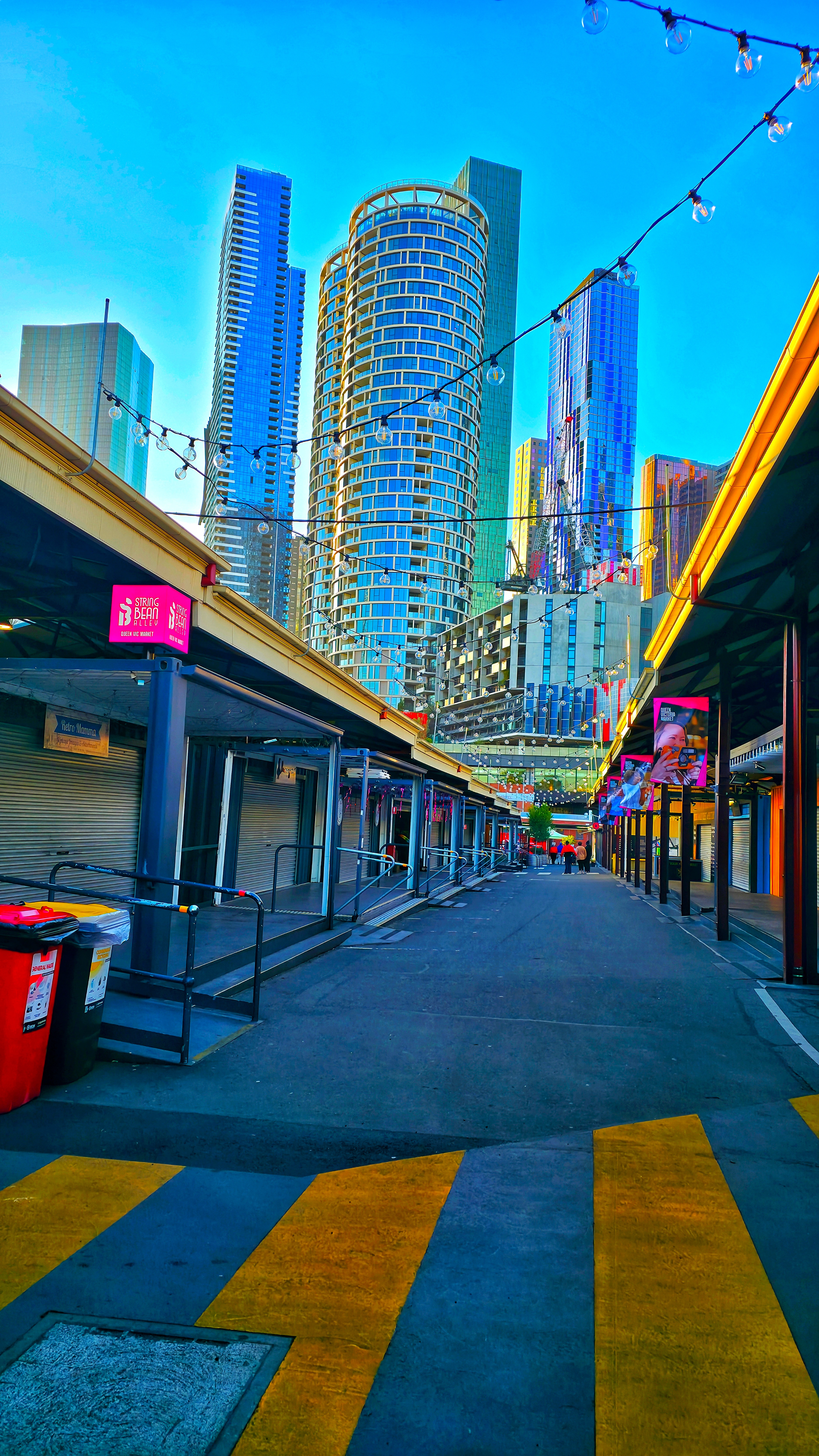Urban street view with modern glass skyscrapers and colorful market stalls under blue sky